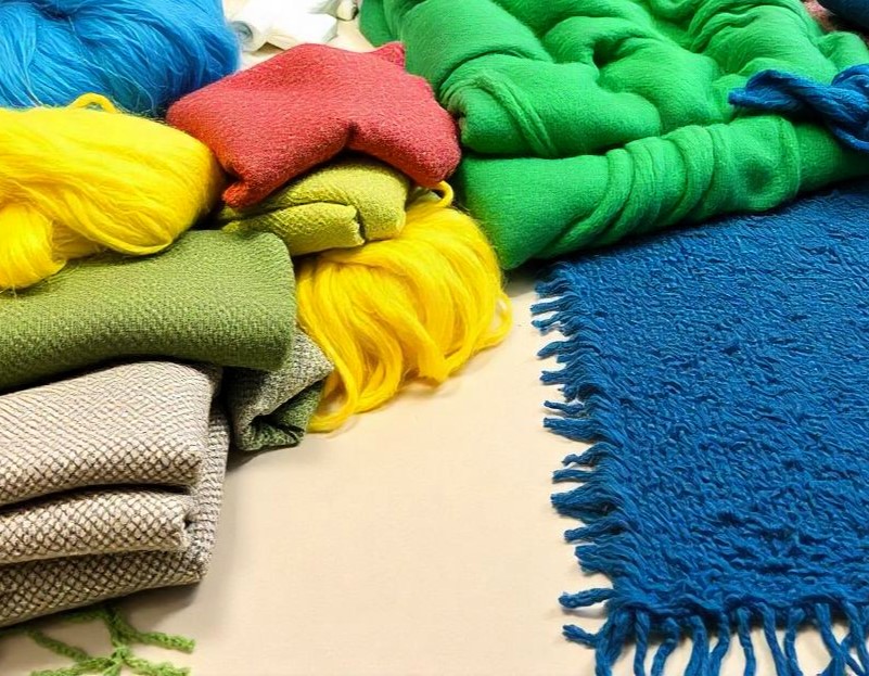 Ovillos de lana en colores vibrantes: azul eléctrico, verde esmeralda y terracota, junto a muestras de telas