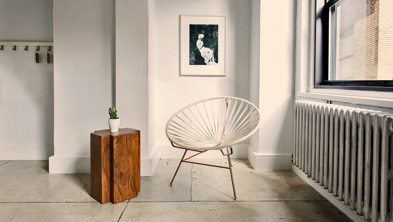 Rincón minimalista con silla de diseño sencillo, mesita de madera, libros, lámpara de mesa y una flor decorativa.
