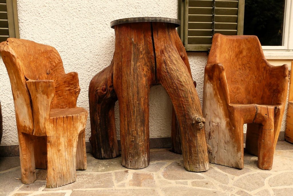 Mesa alta y dos sillas o banquetas altas talladas a partir de un tronco, representando el diseño Raw Luxury en su máxima expresión.