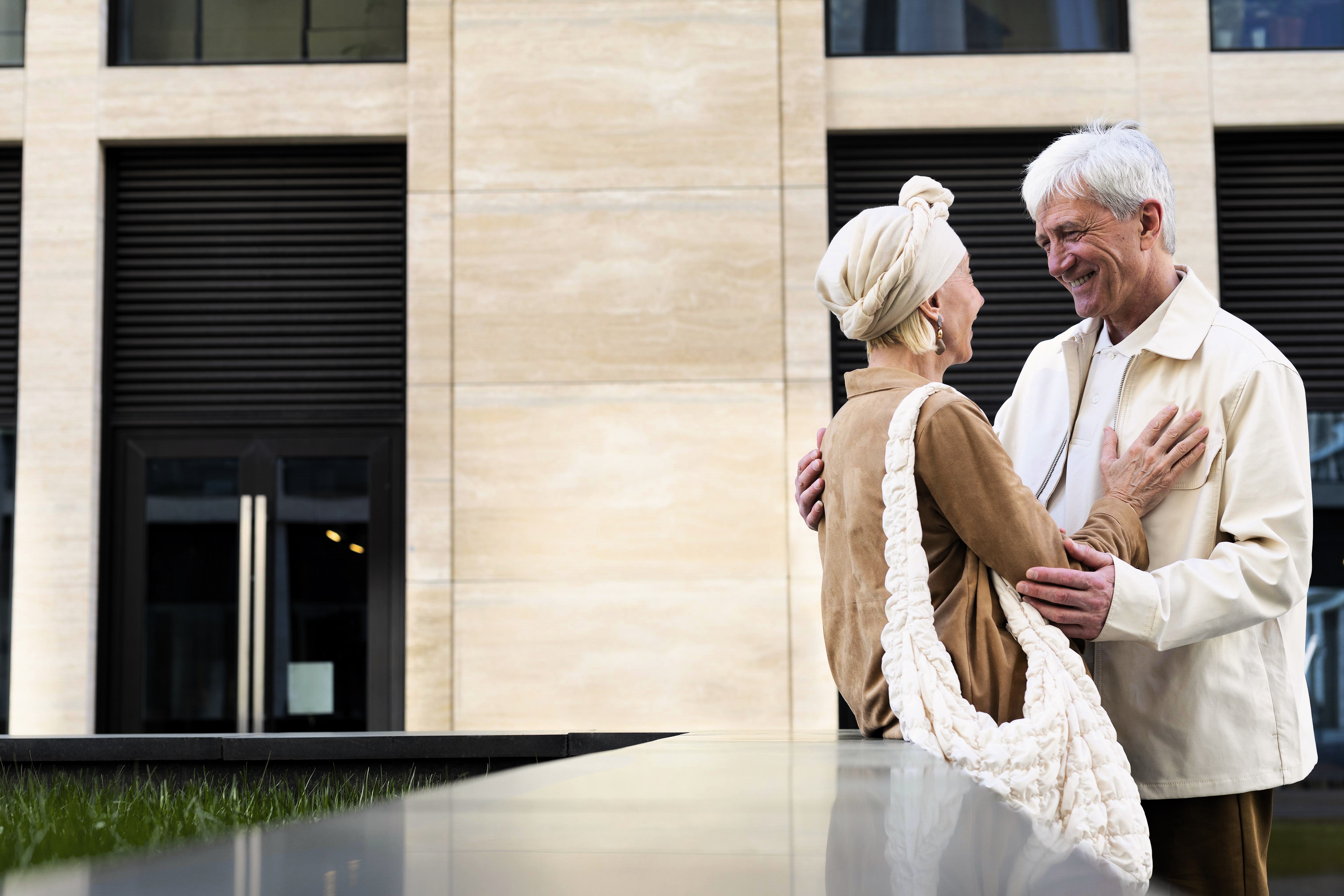 Pareja de mayores sonrientes frente a un elegante edificio moderno, Espacios Senior Living