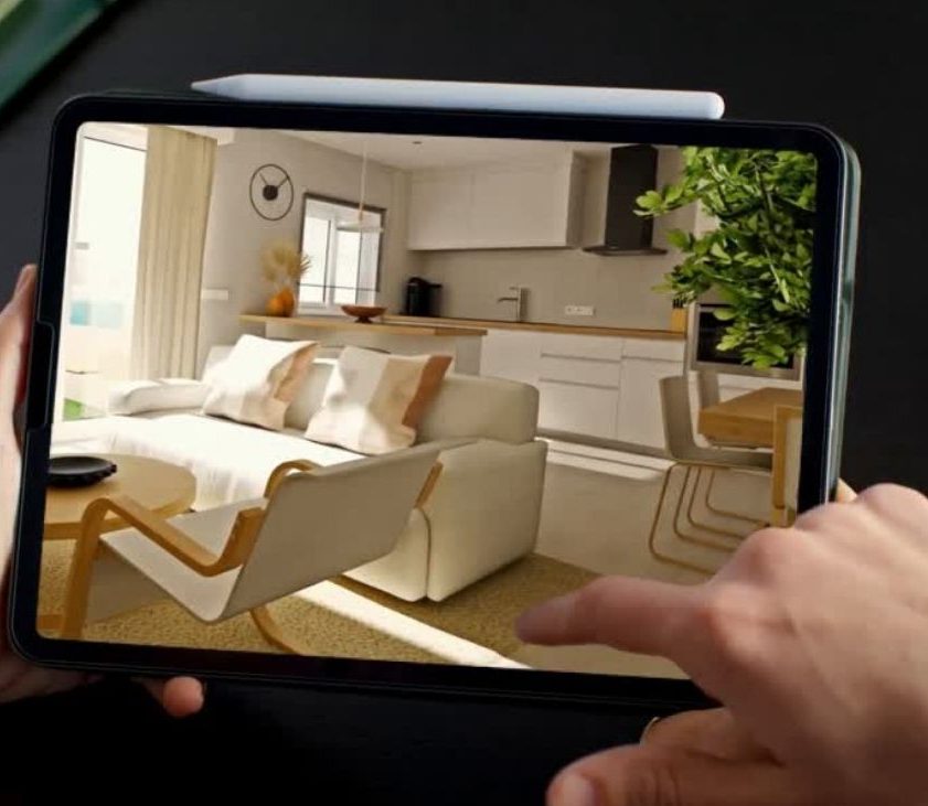 Render 3D de un espacio abierto con cocina, salón y comedor mostrado en la pantalla de una tablet sobre una mesa de diseño minimalista